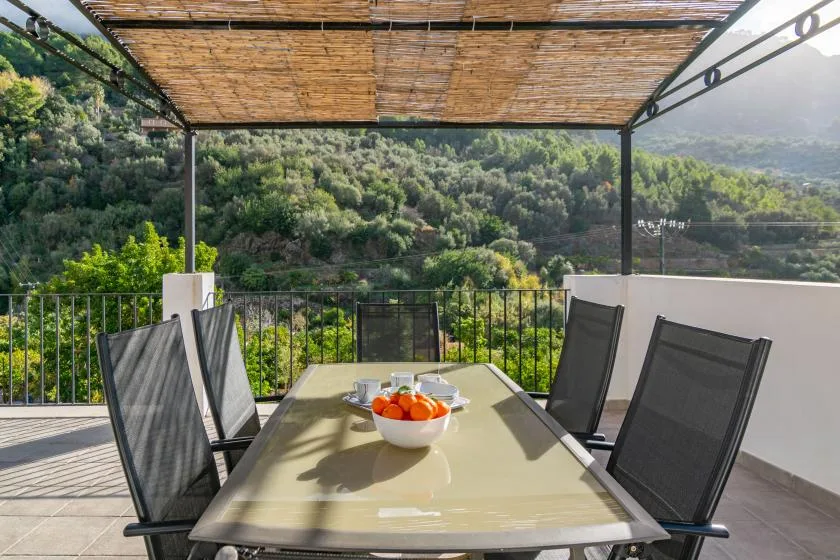An outdoor dining area with a table and seating beneath a shaded pergola.