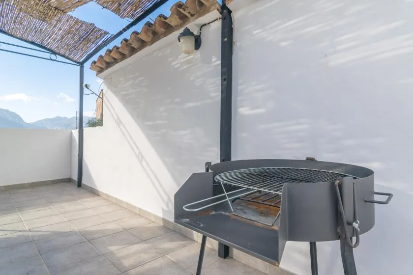 Una terraza exterior embaldosada con una parrilla metálica junto a una pared blanca.