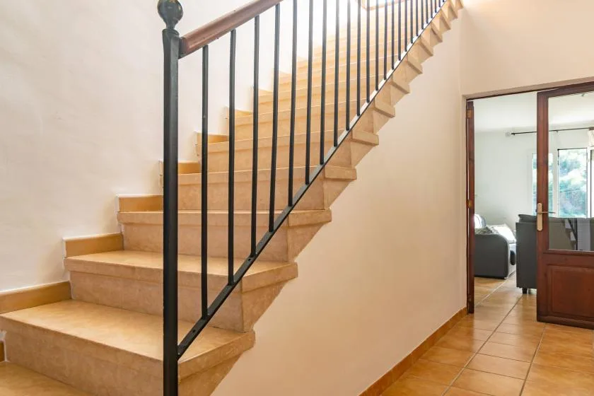 Una escalera interior con peldaños beige y una barandilla de metal oscuro.