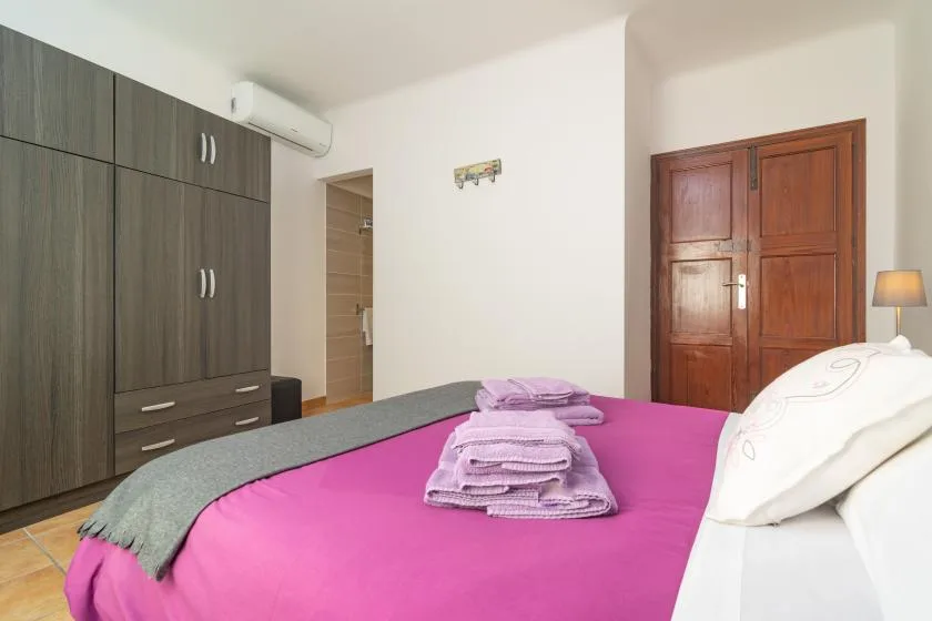 Un dormitorio con una cama cubierta de ropa de cama rosa y un armario de madera.