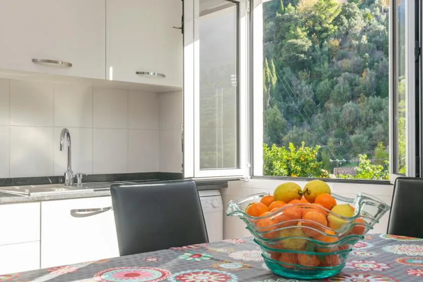 Una cocina luminosa con un frutero sobre la mesa junto a una ventana grande.