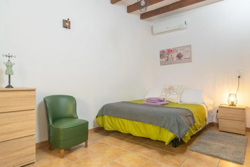 Un dormitorio con una cama, asientos verdes y vigas de madera en el techo.