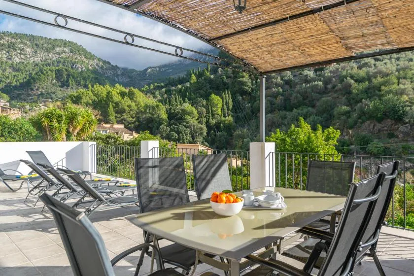 An outdoor dining terrace with a table and seating overlooking a green mountain valley.