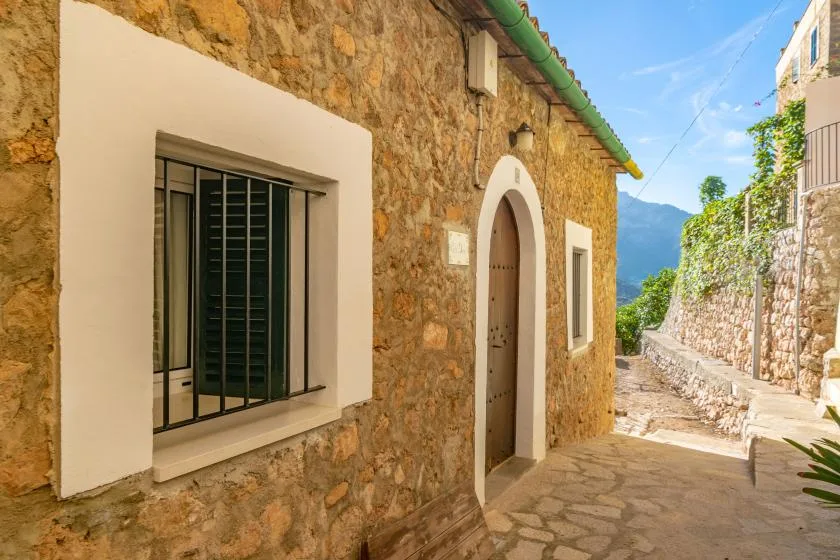 El exterior de una casa de piedra da a un estrecho camino pavimentado bajo un cielo despejado.
