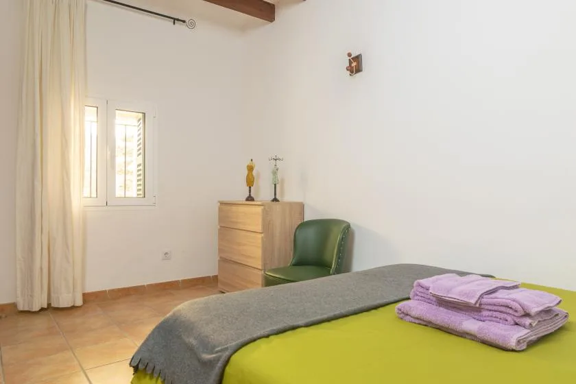 Un dormitorio con una cama, una cómoda pequeña y una ventana junto a las cortinas.