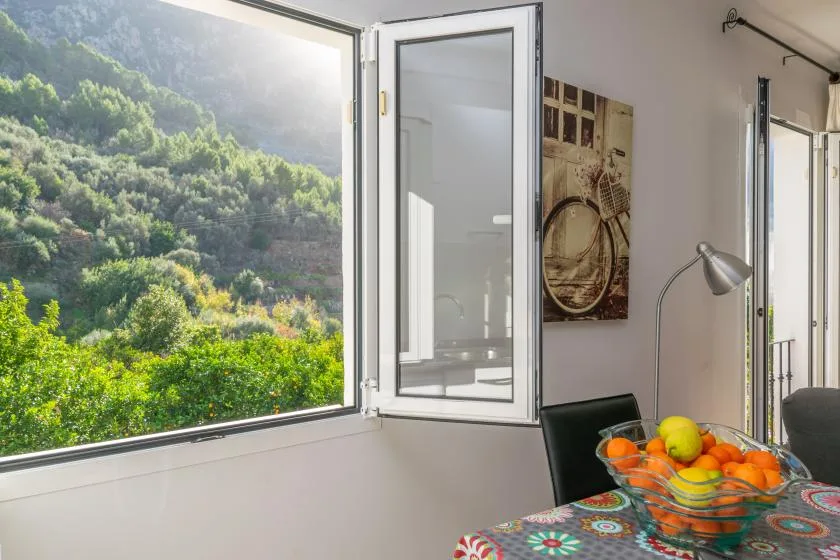 Un comedor luminoso con una ventana abierta frente a una ladera verde.