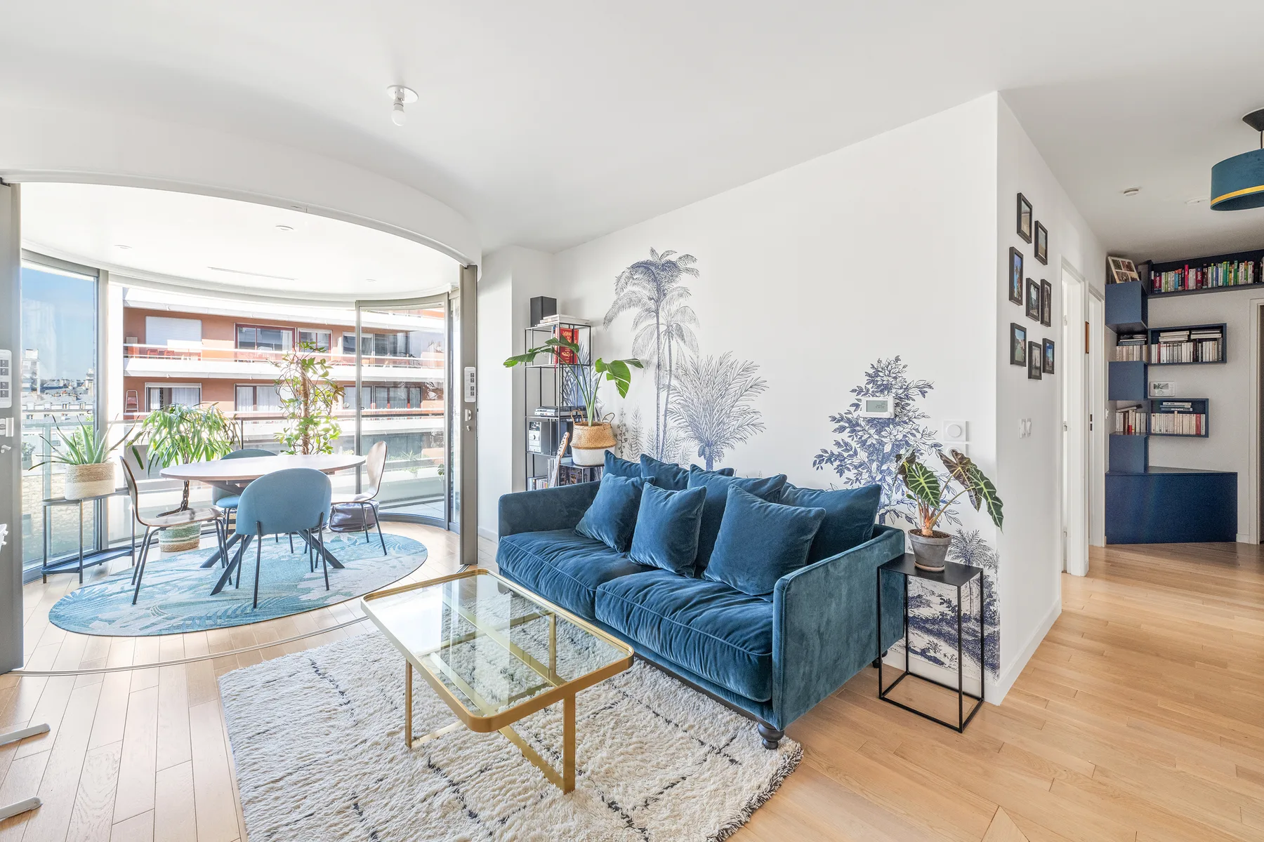 Una sala luminosa con asientos azules y un comedor junto a grandes ventanales.
