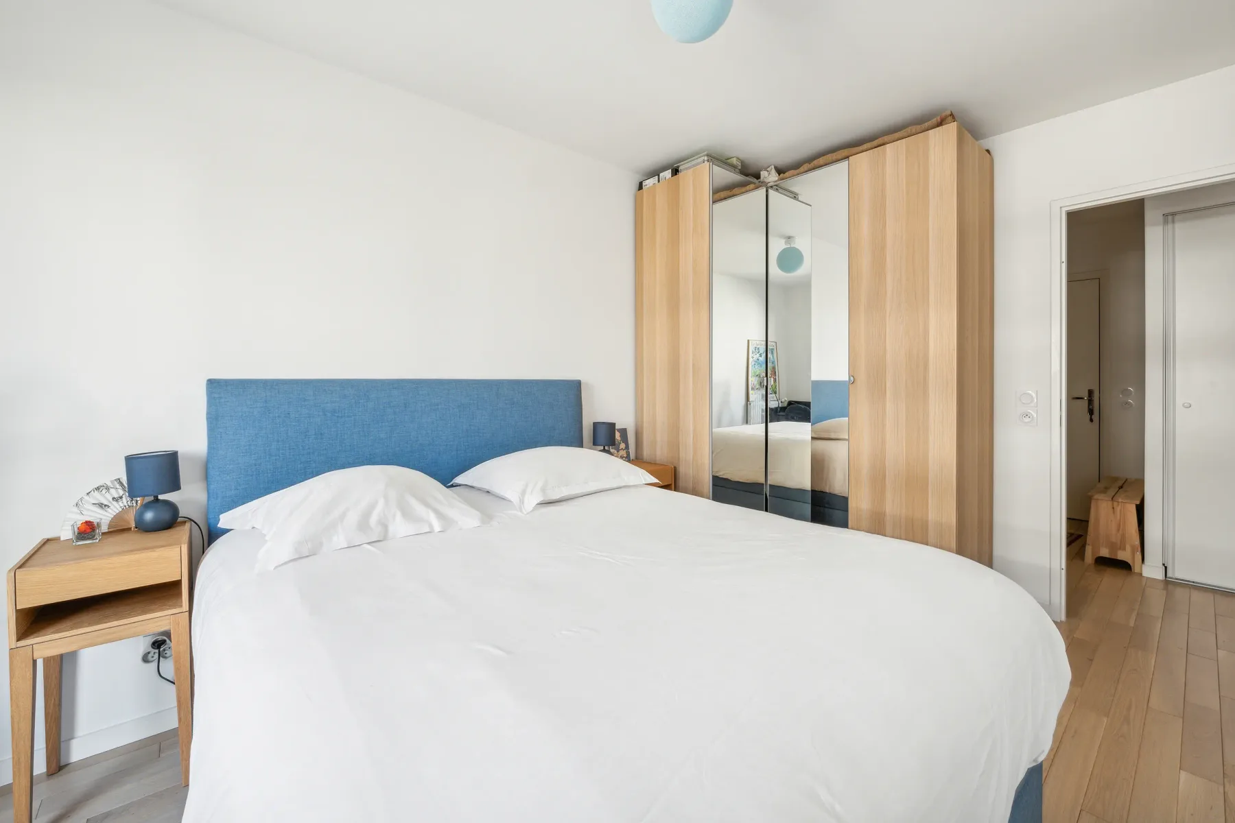 Un dormitorio con una cama grande, un cabecero azul y un armario con espejo.