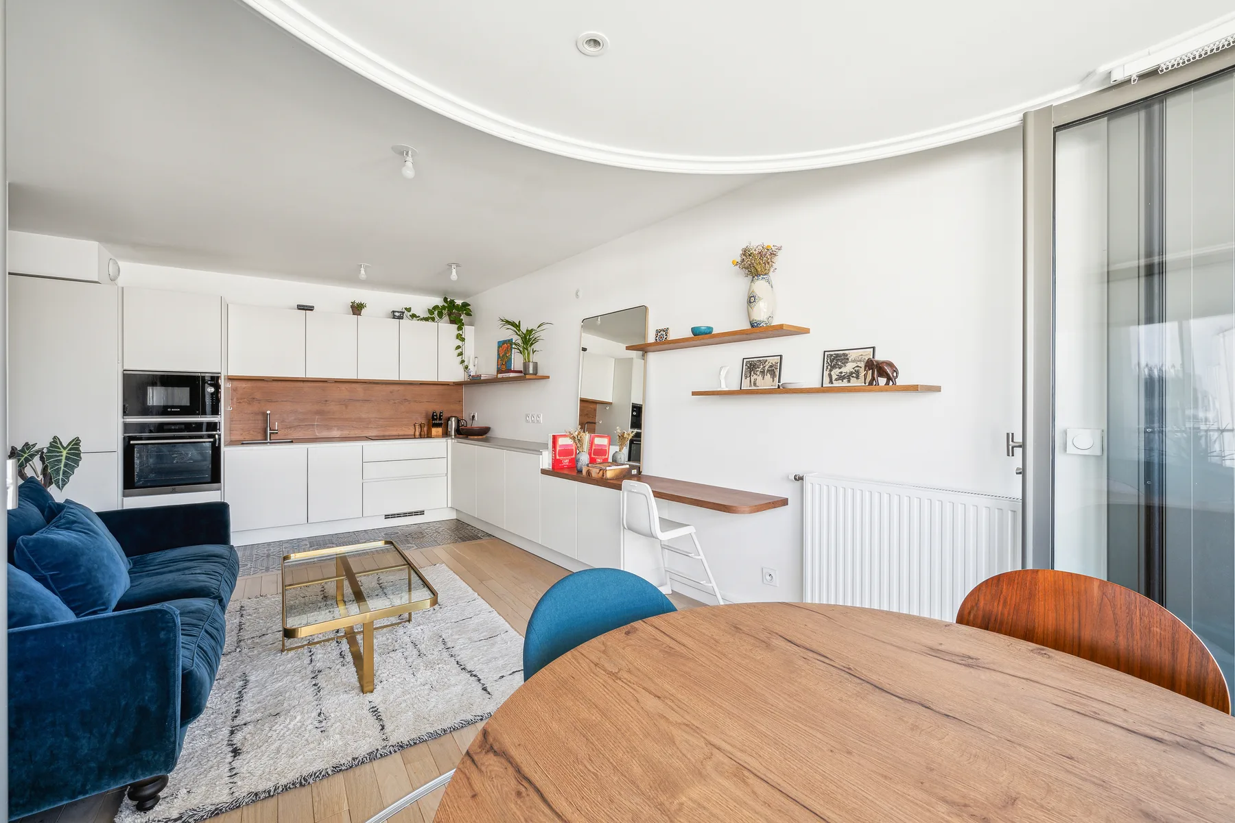 Una cocina abierta al salón, con mesa de comedor y asientos azules.