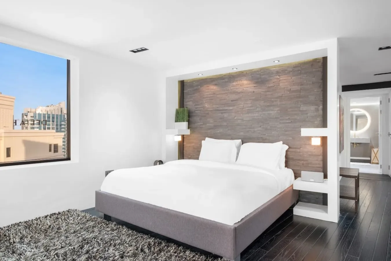 Un dormitorio luminoso tiene una cama frente a una pared revestida de madera y una ventana grande.