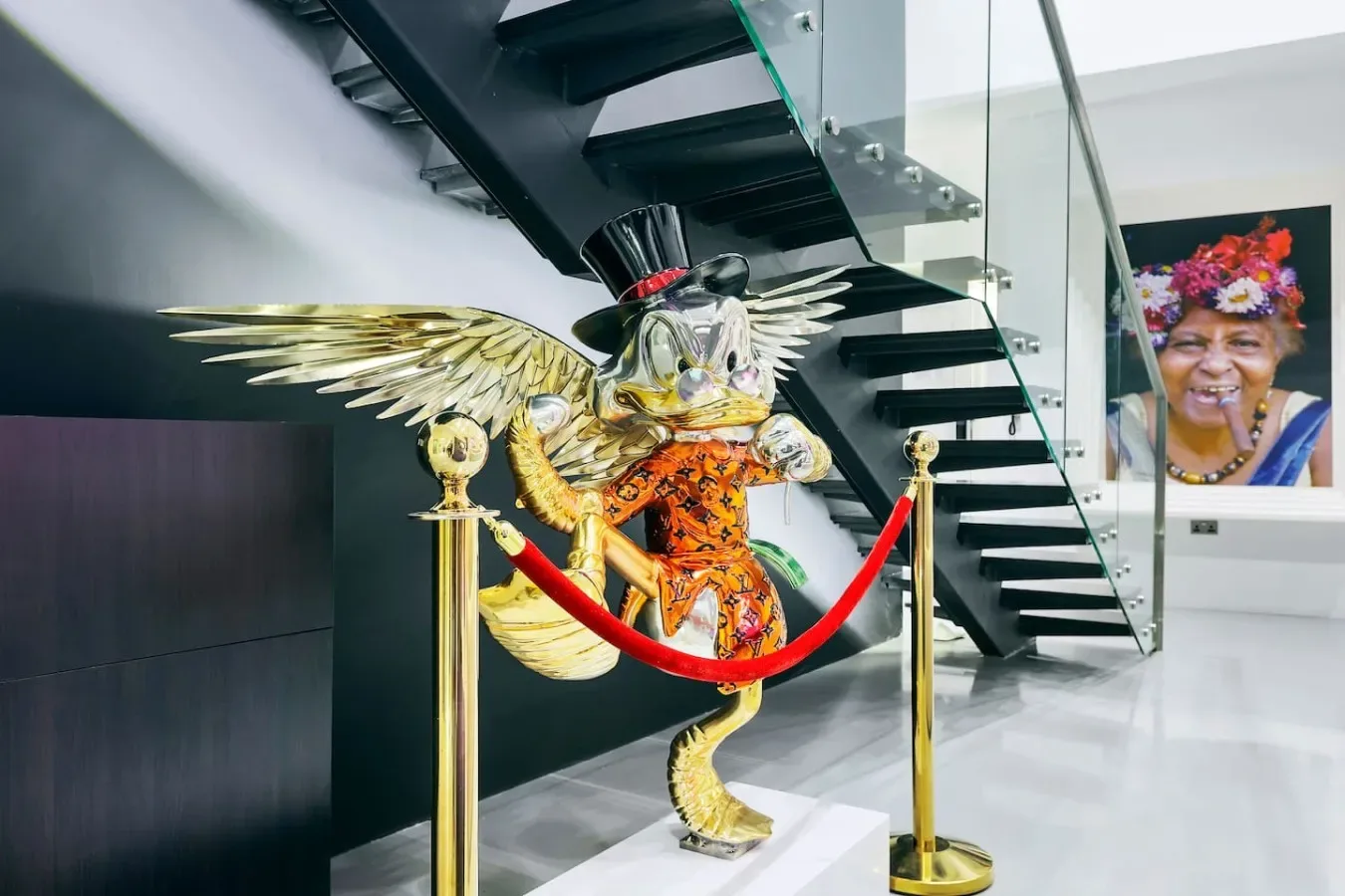 Una colorida escultura alada está detrás de una barrera de cuerda roja bajo una escalera.