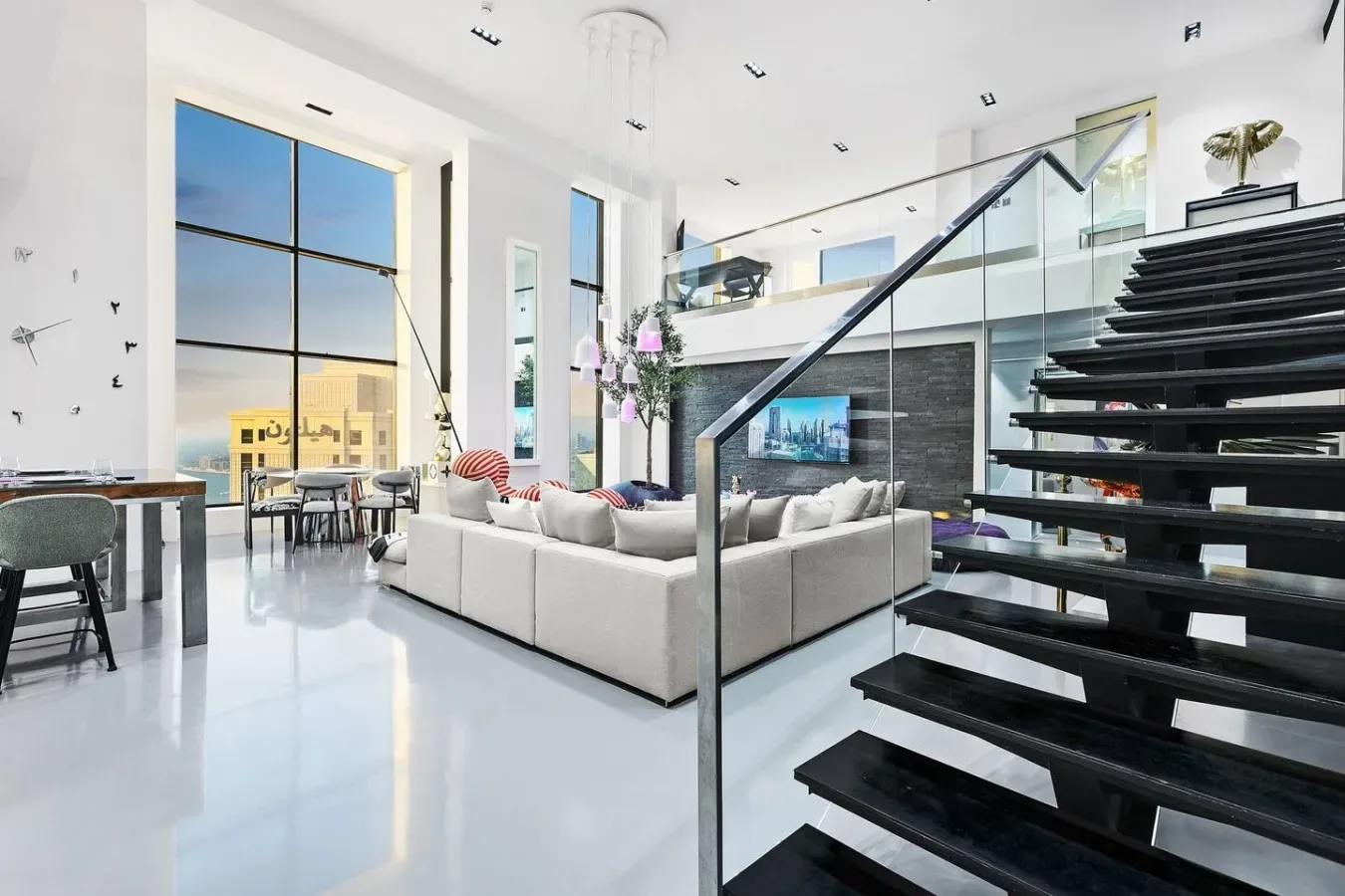 Una sala de estar luminosa con asientos junto a grandes ventanas y una escalera abierta.