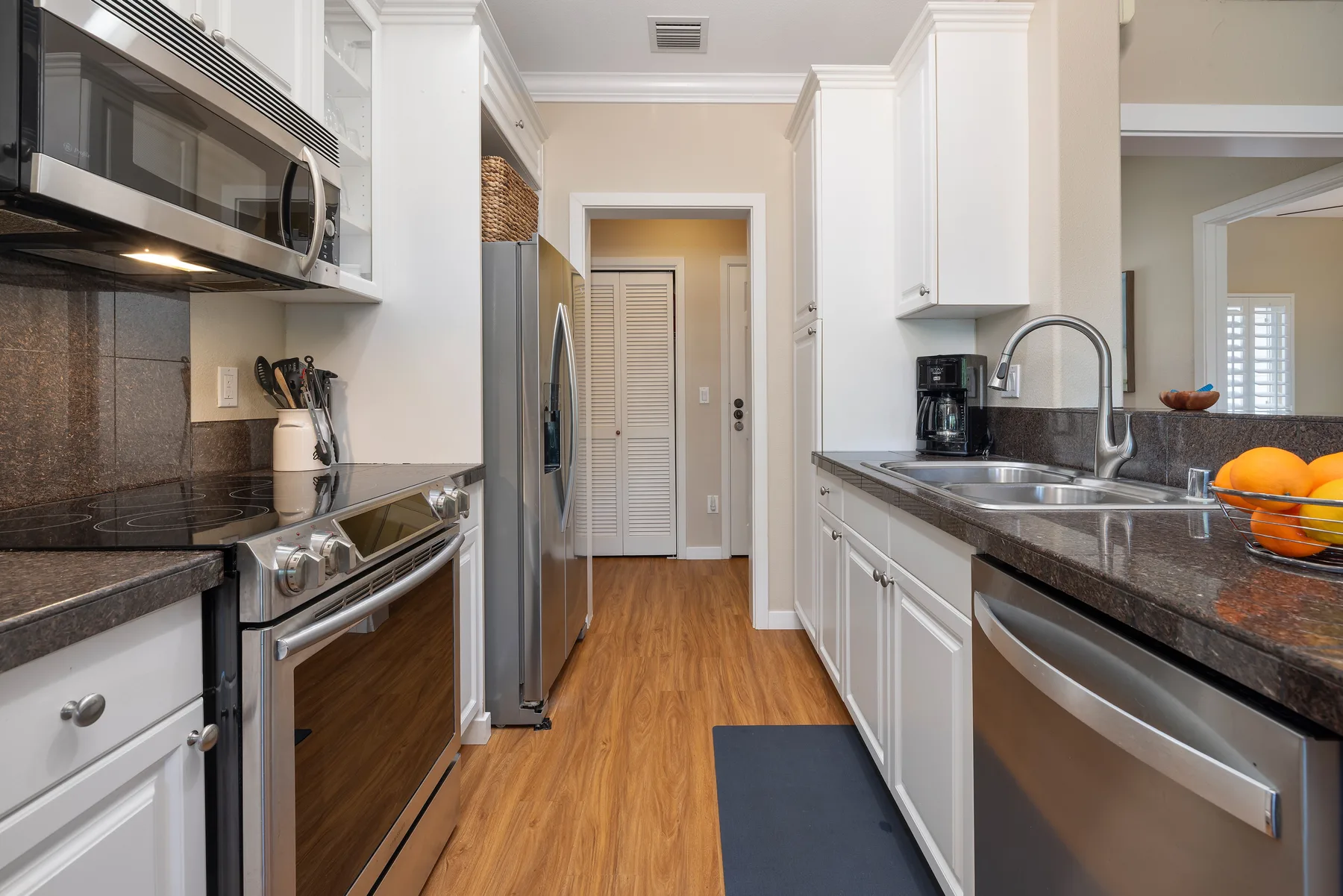 Una cocina tipo pasillo luminosa con gabinetes blancos, electrodomésticos de acero inoxidable y un pasillo central.