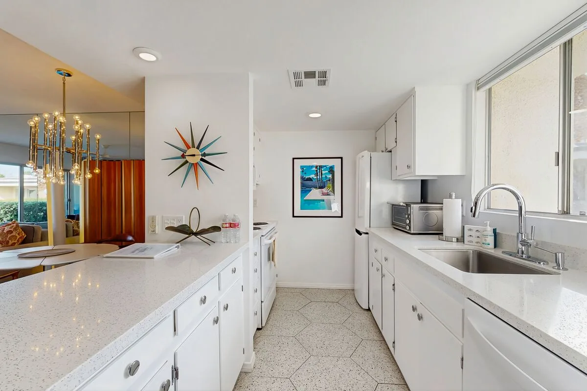 A bright kitchen with white counters and a sink beneath a large window.