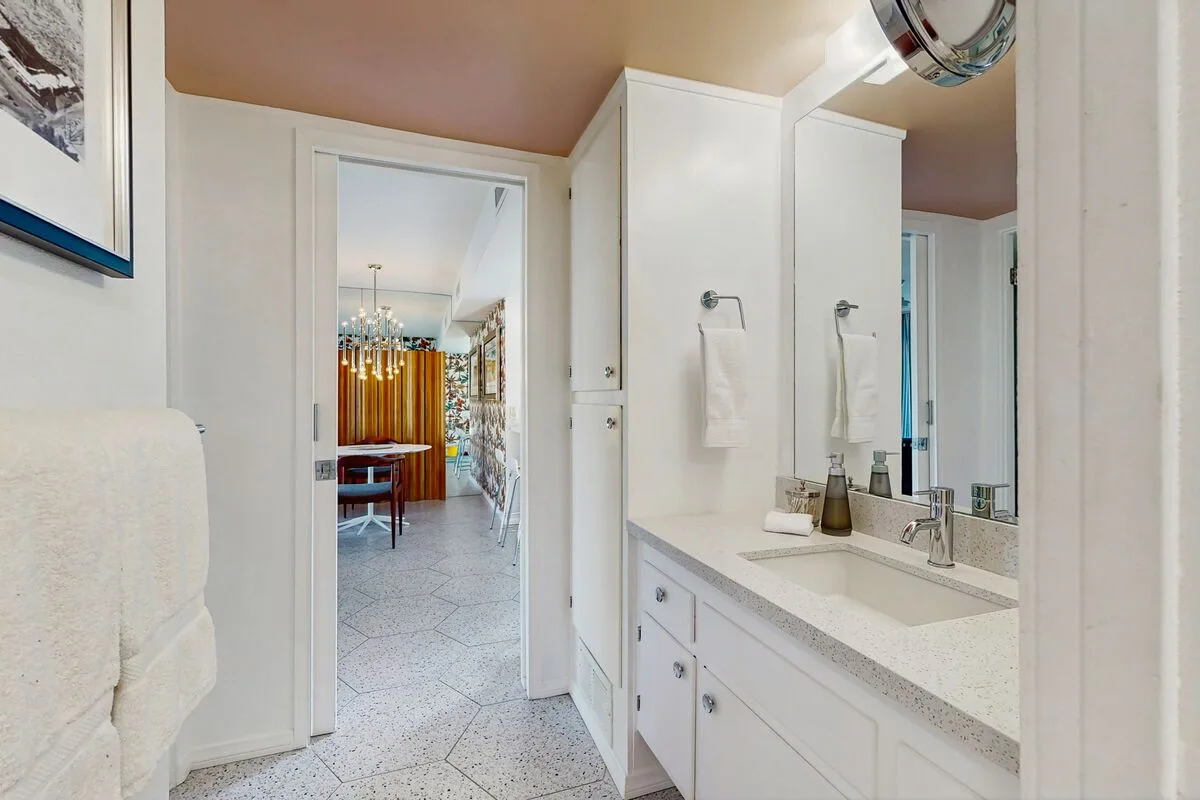 A bright bathroom with a long vanity and an open doorway to the adjoining room.