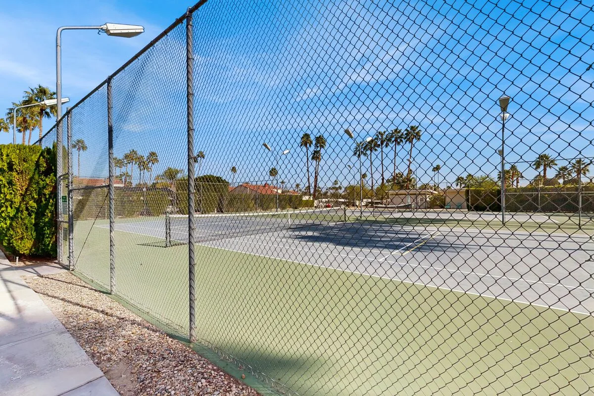 A fenced outdoor tennis court with palm trees in the background.