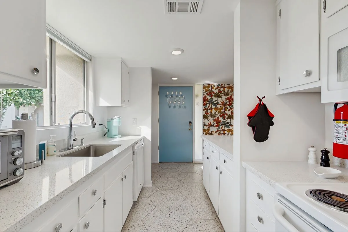 A bright kitchen with white cabinets, long countertops, and a blue door.