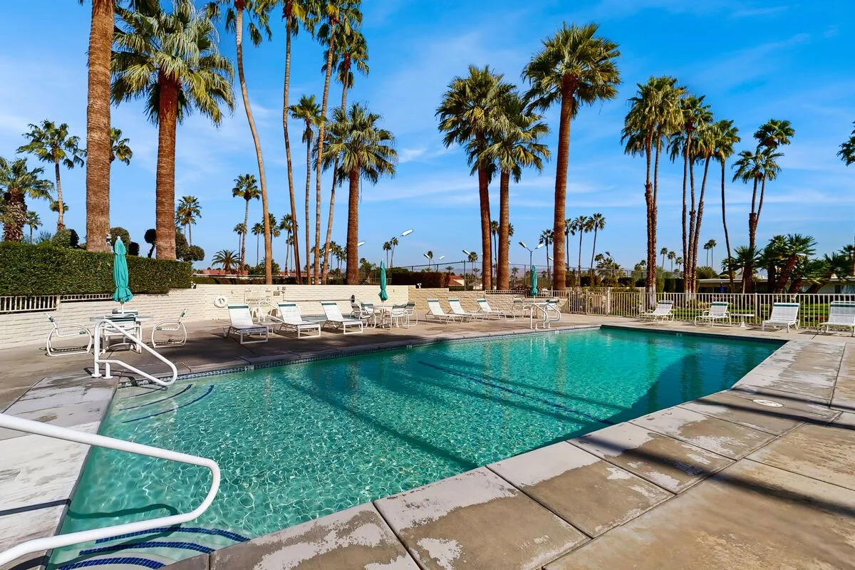 An outdoor swimming pool is surrounded by palm trees and lounge chairs.
