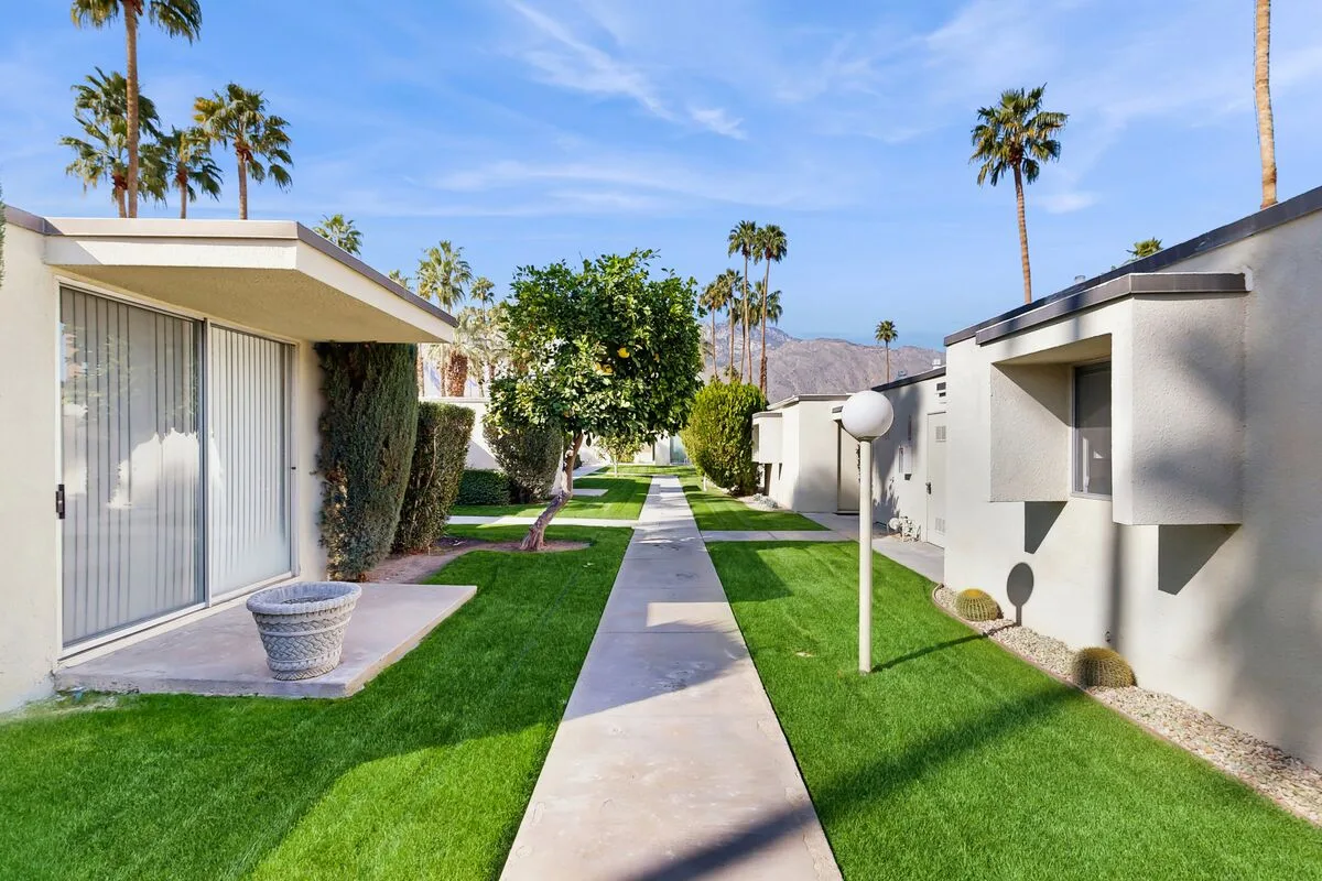 A landscaped walkway runs between low modern buildings, with palm trees in the background.