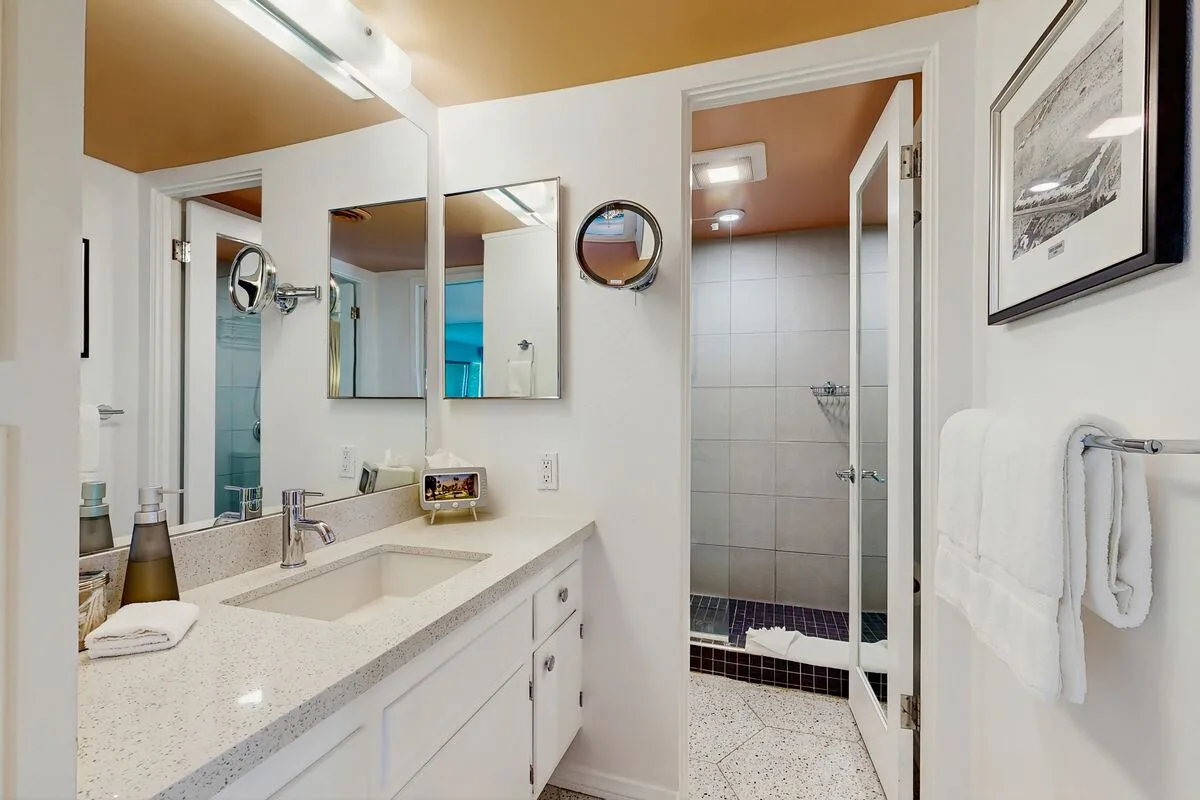 A bathroom vanity with a sink and mirror beside a tiled shower.