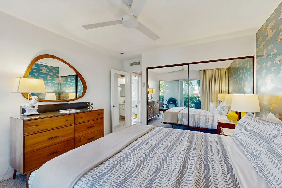 A bright bedroom with a large bed, wooden dresser, and sliding glass doors.