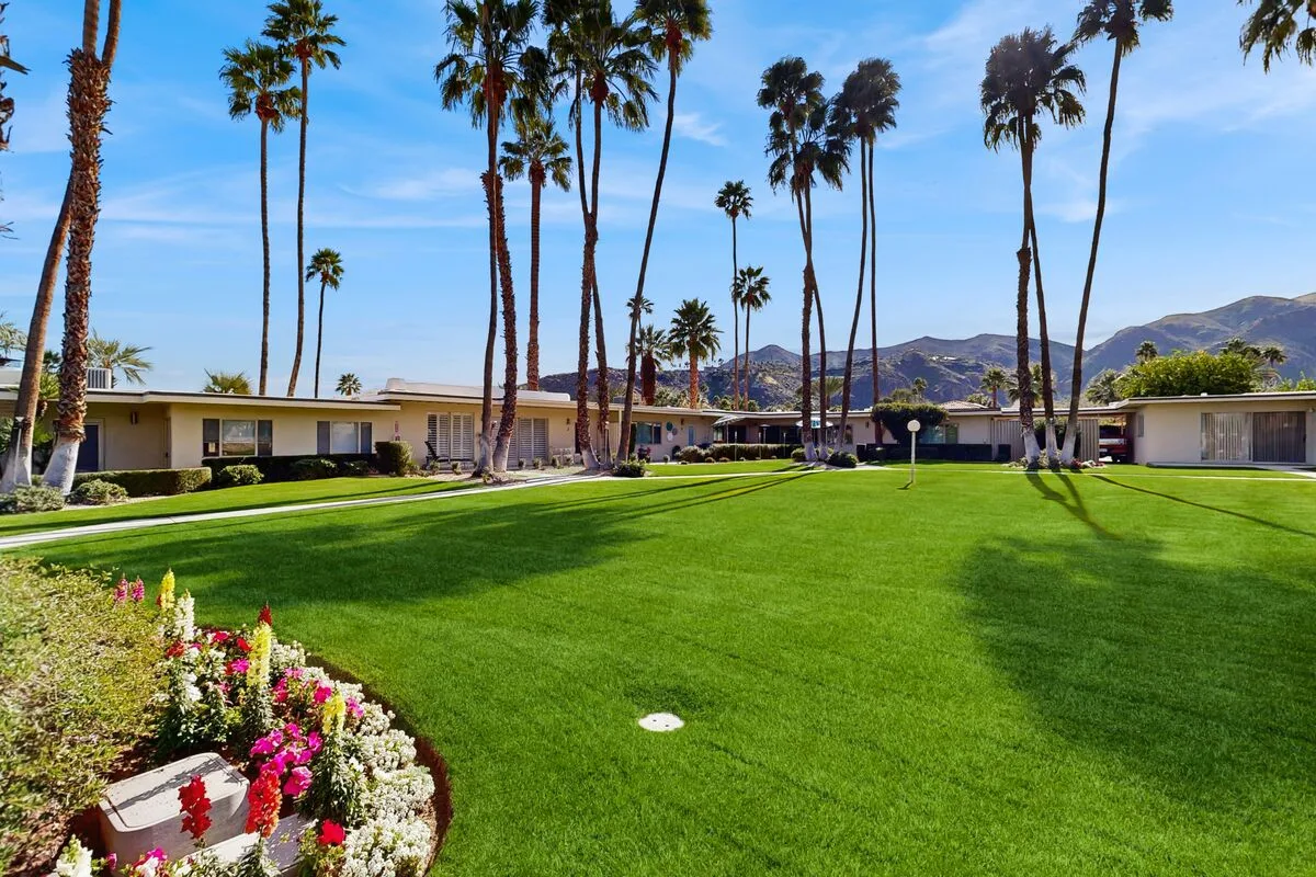 A landscaped lawn with palm trees and low buildings beneath distant hills.