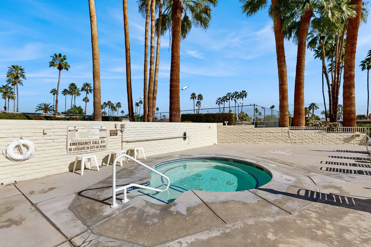 A small outdoor swimming pool sits beside a paved deck lined with palm trees.