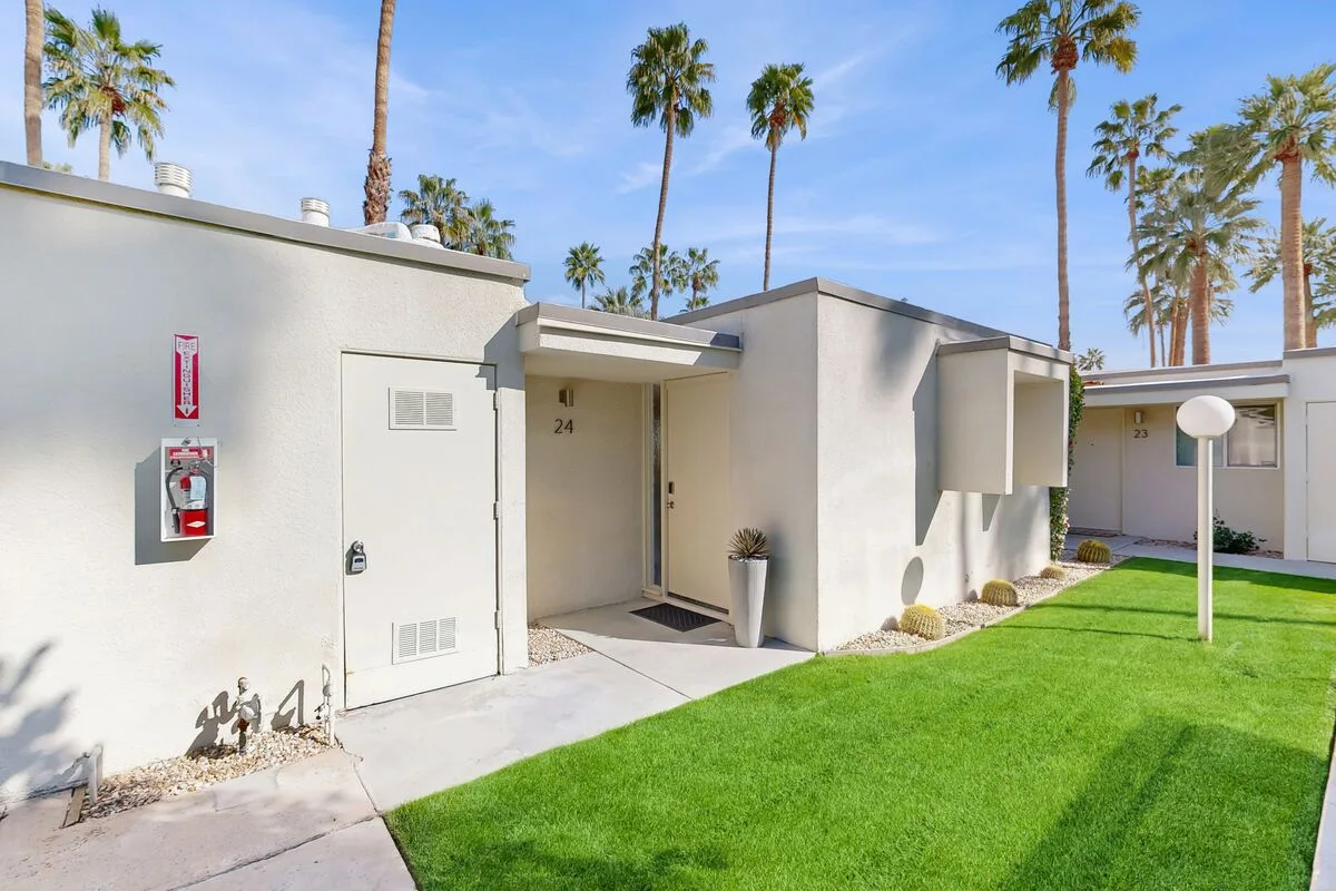 A low white building entrance opens onto a lawn lined with palm trees.