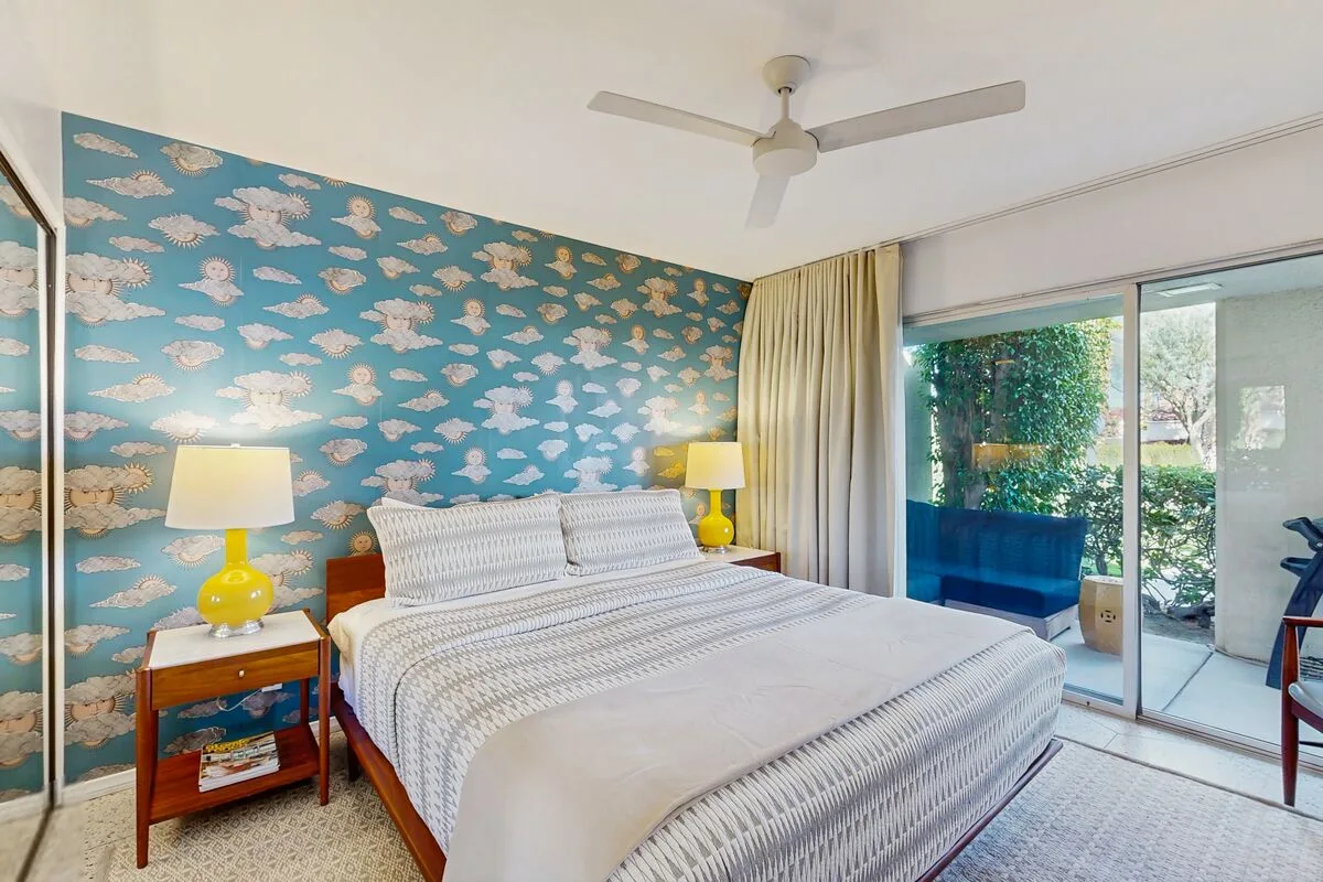 A bedroom with a bed beside a blue patterned wall and sliding glass doors.