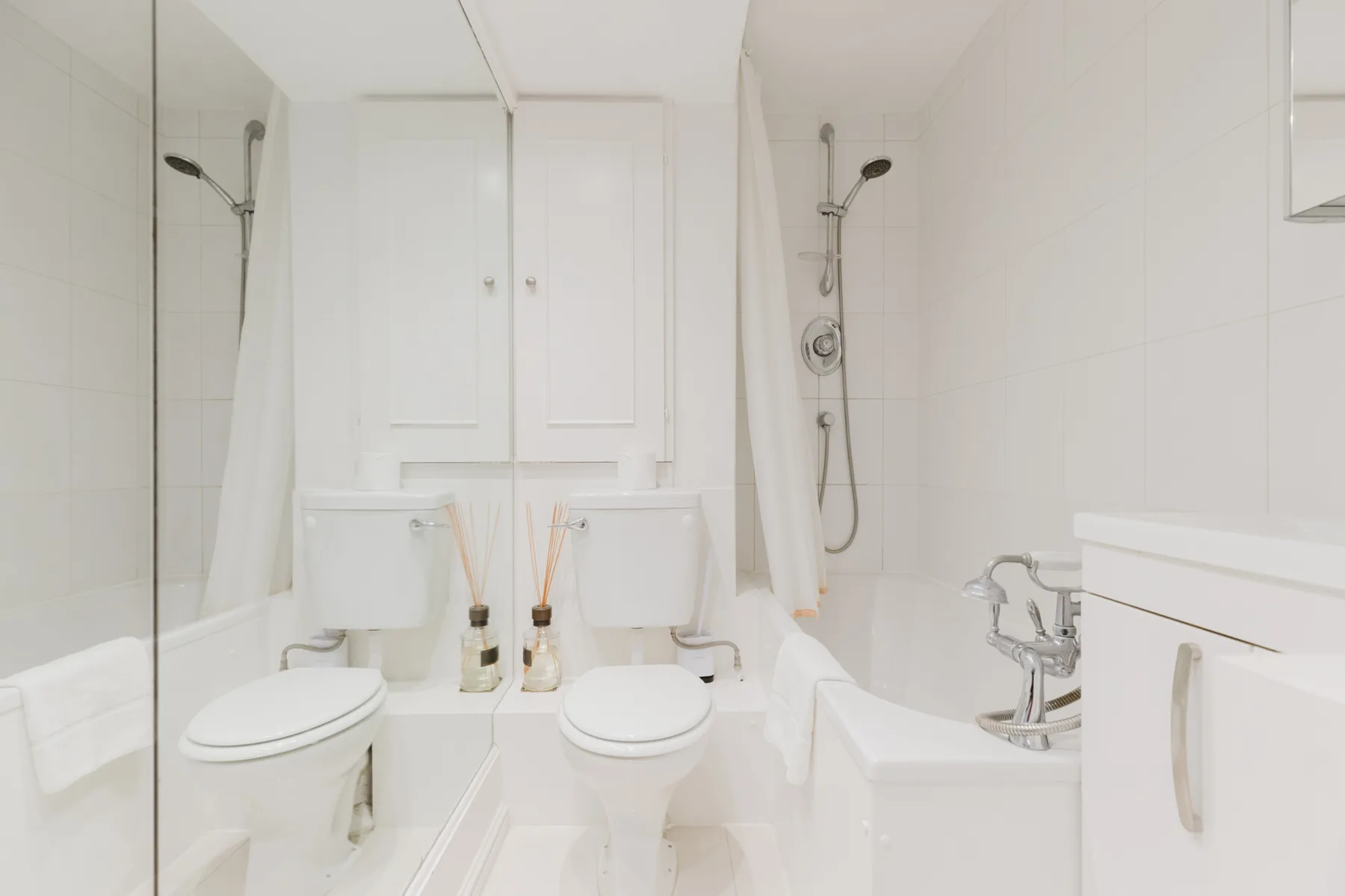 A bright bathroom with two toilets and a bathtub.