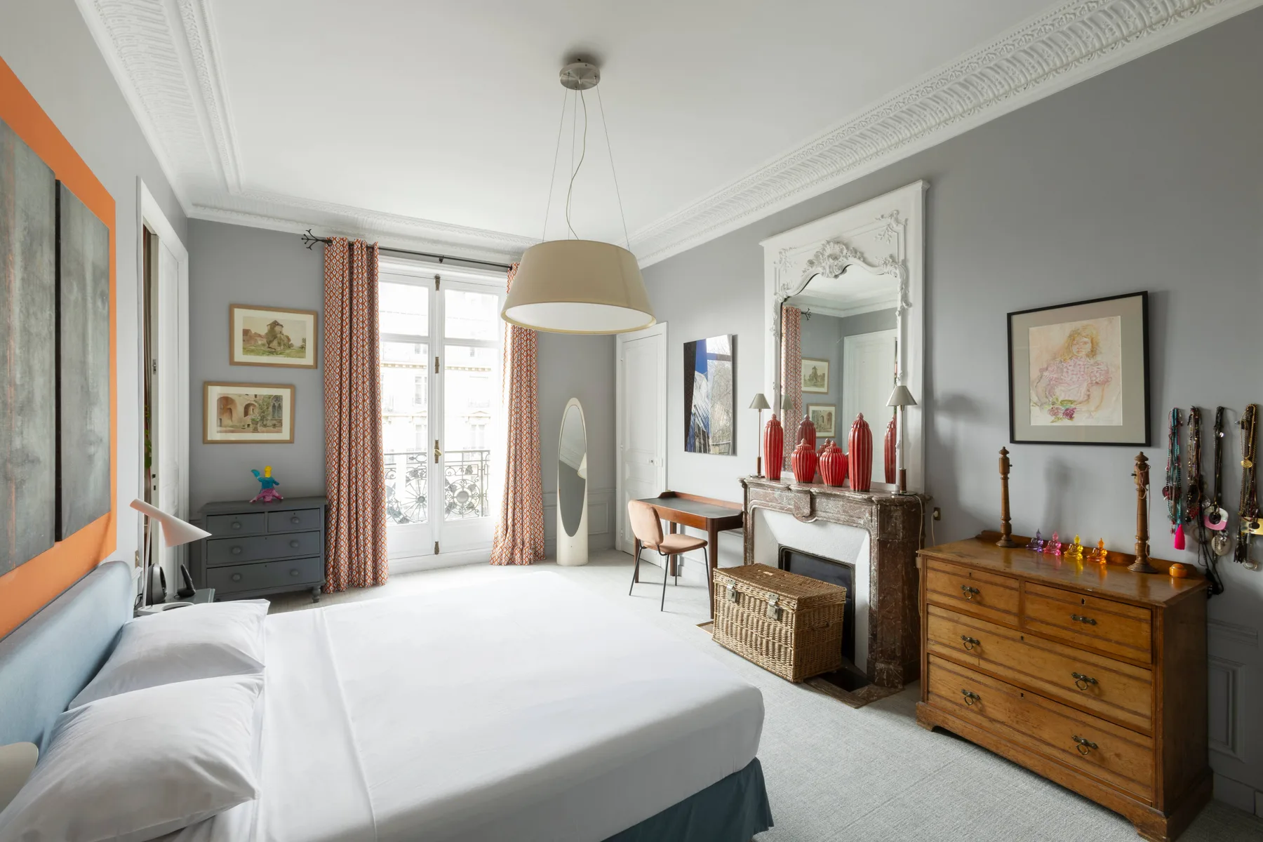 A bright bedroom with a bed, a fireplace, and a tall mirror.
