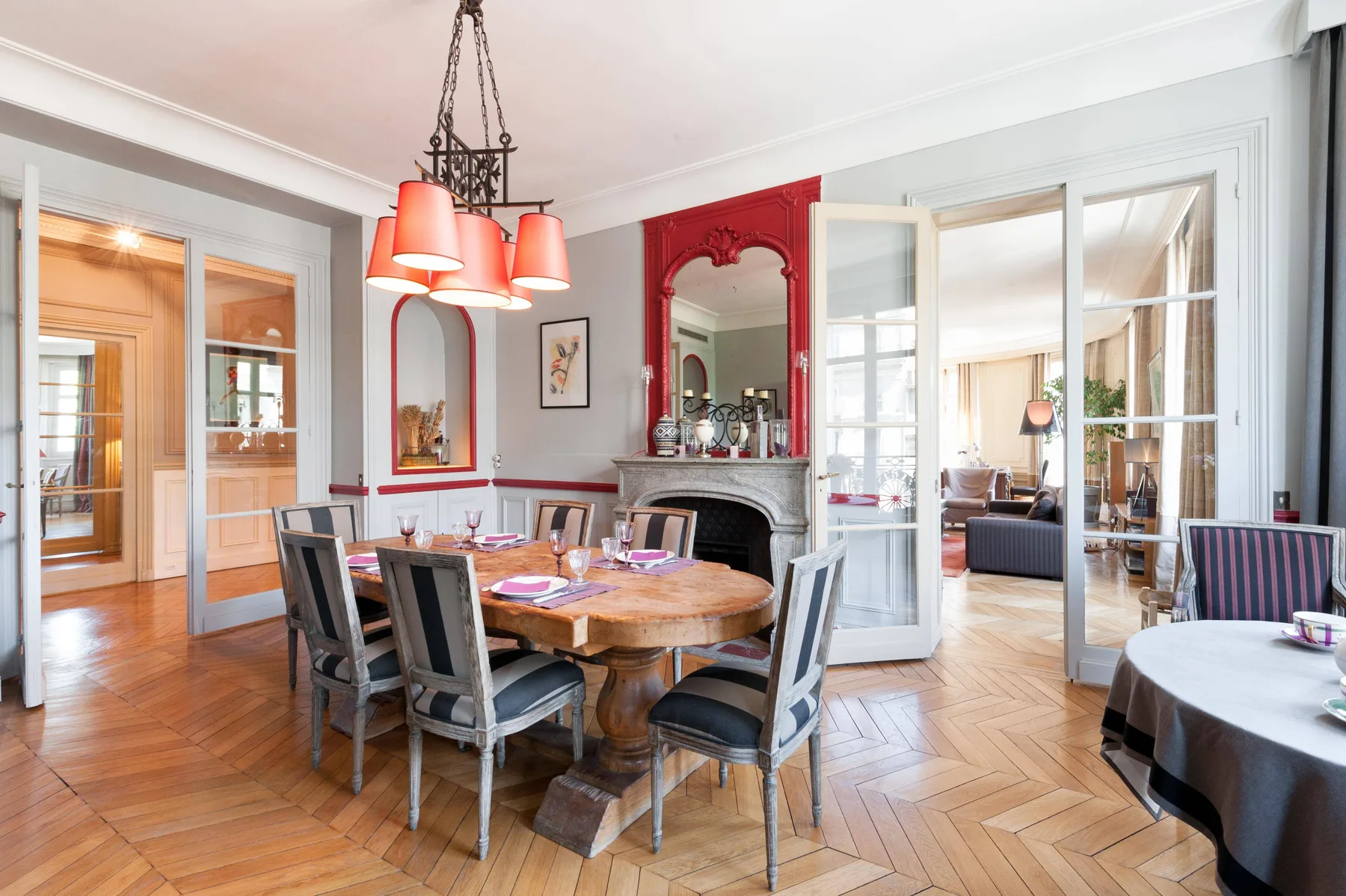 A dining room with a wooden table and open doors leading to a sitting area.