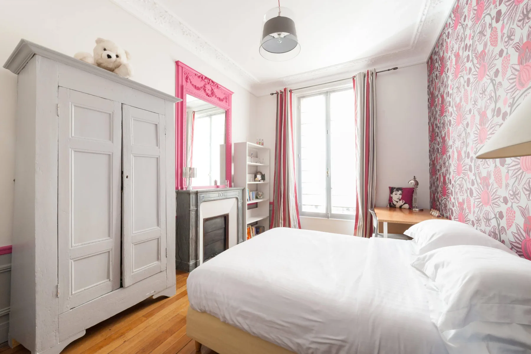 Un dormitorio luminoso con una cama blanca, un armario alto y una ventana grande.