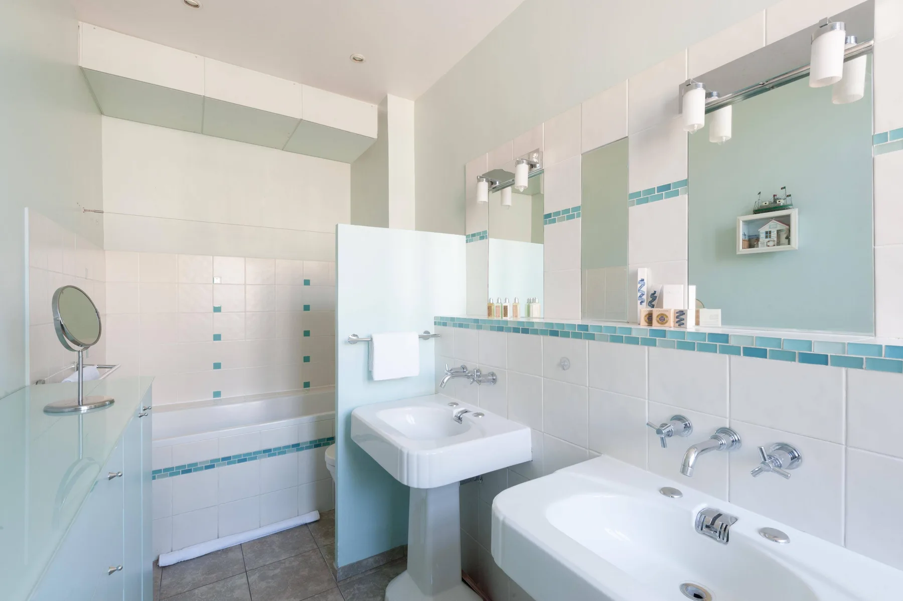 Un baño luminoso con azulejos, bañera, dos lavabos y espejos grandes.