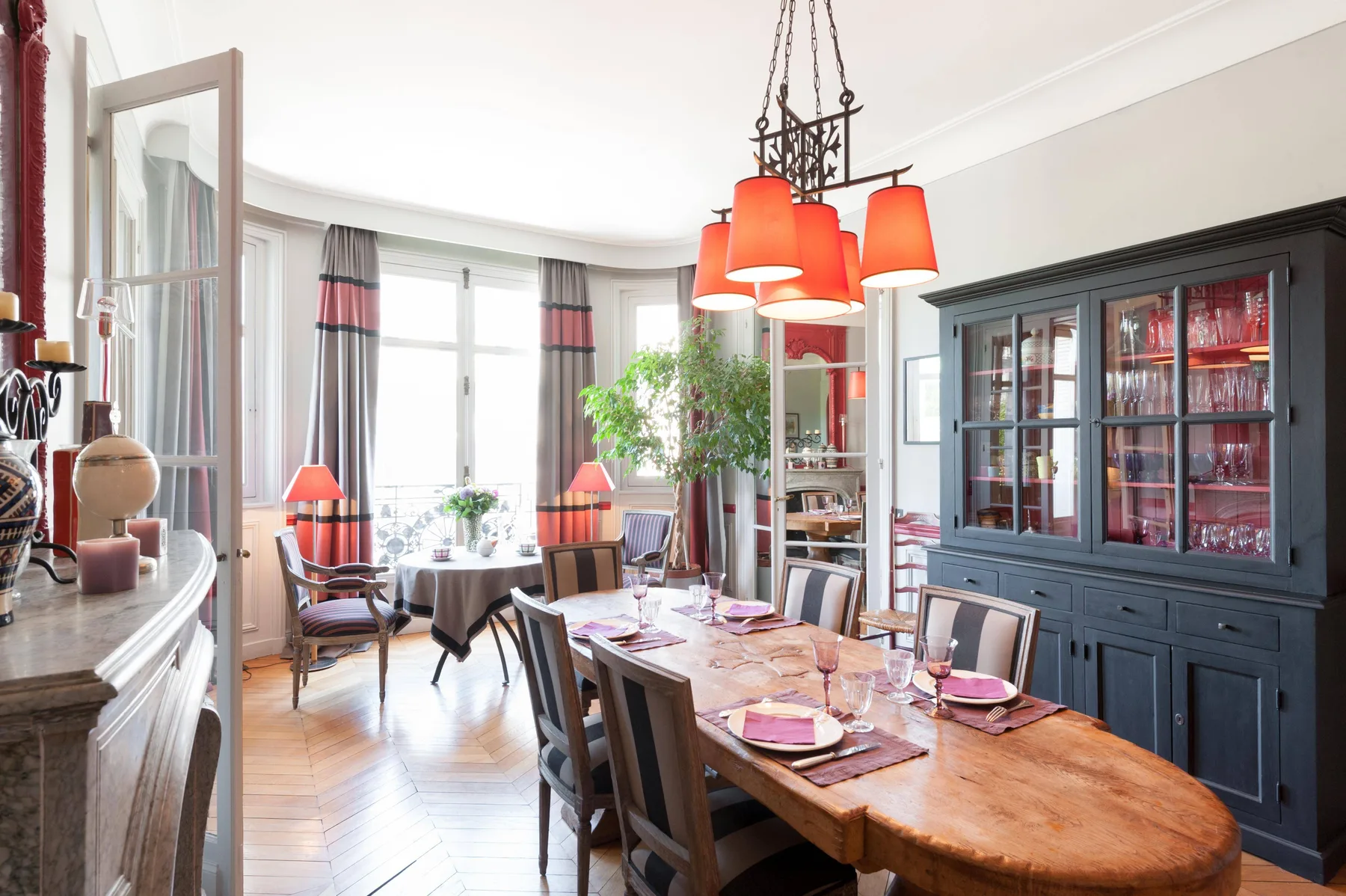 Un comedor con una larga mesa de madera bajo lámparas colgantes rojas.