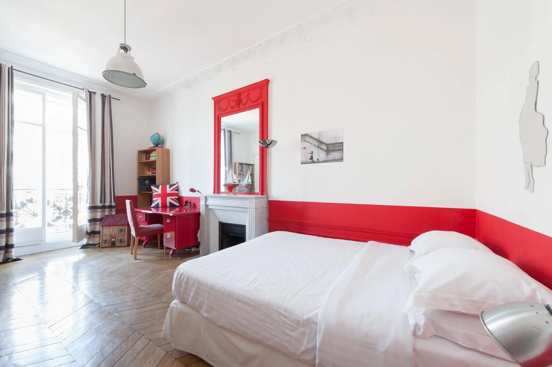 Un dormitorio luminoso con una cama blanca y un escritorio junto a la ventana.