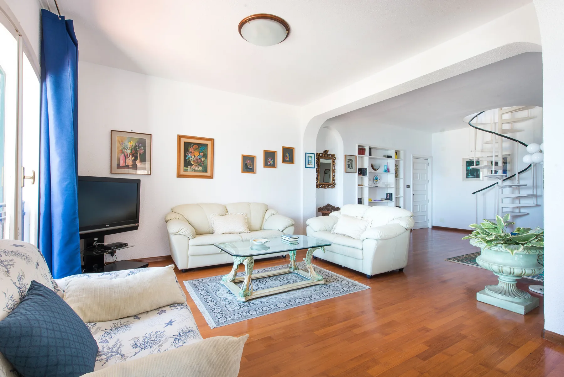 A bright living room with white seating, a glass coffee table, and a television.