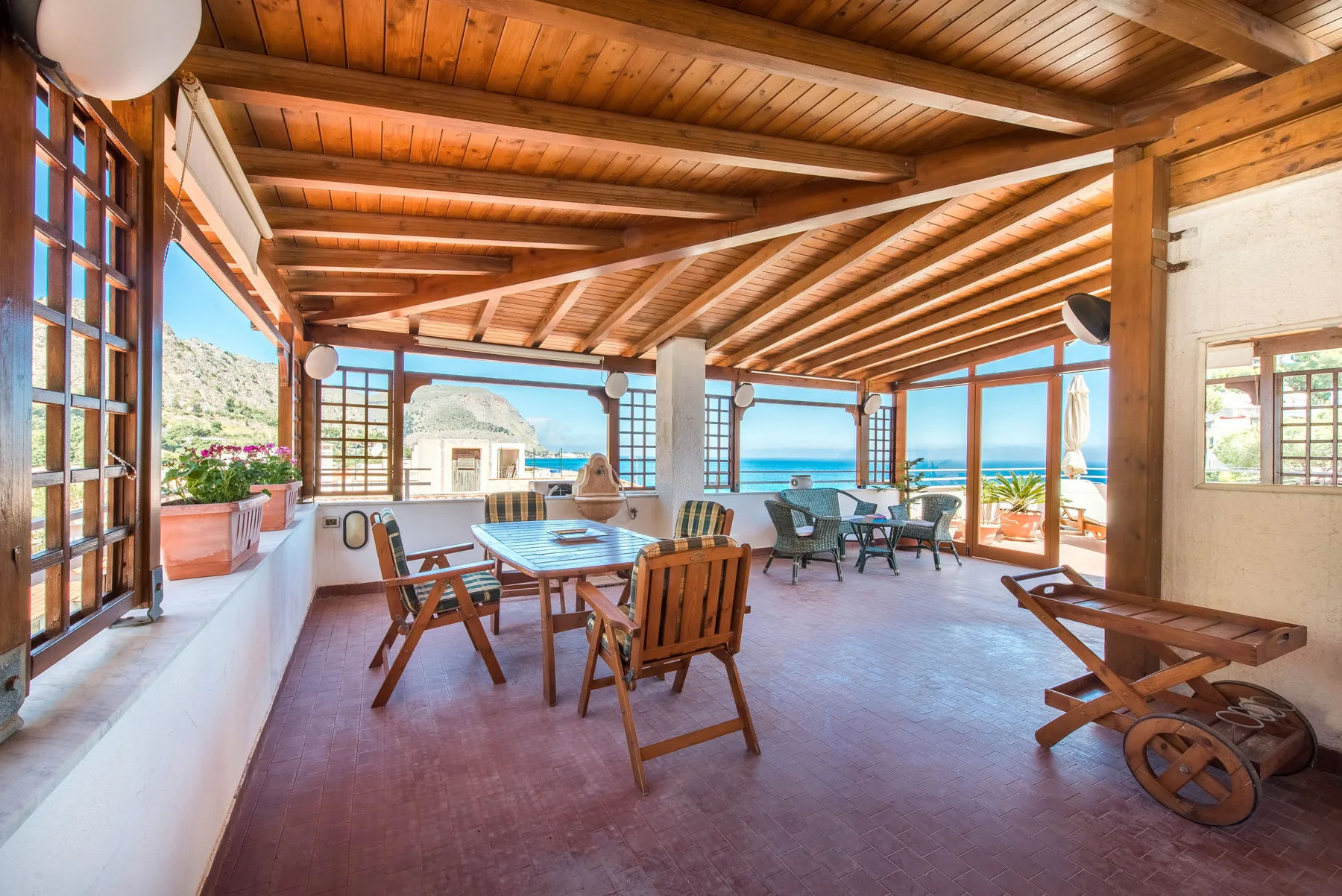 A covered open-air dining area with wooden tables and a sea view.
