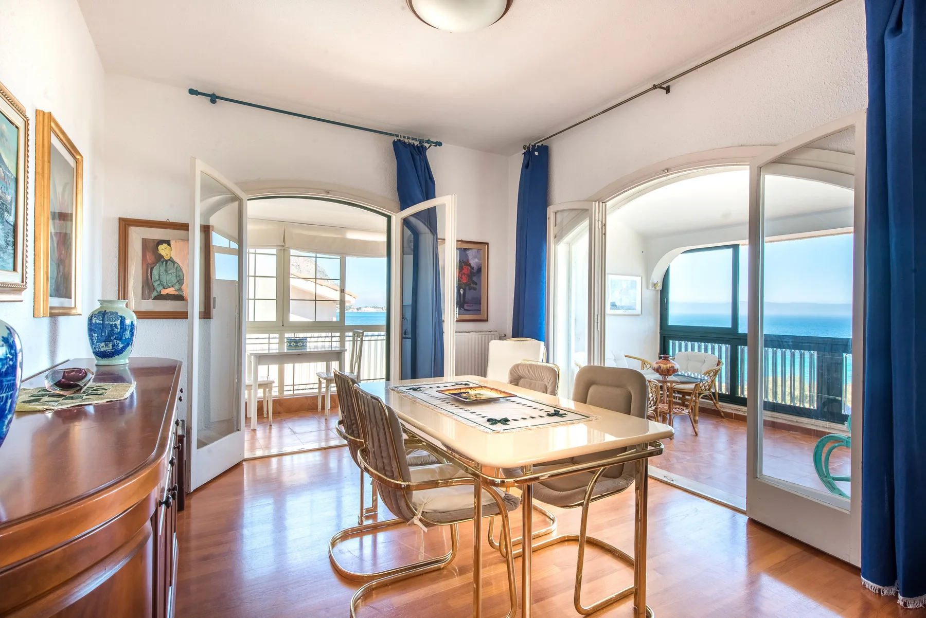 A dining area with a table and seating beside open doors overlooking the sea.