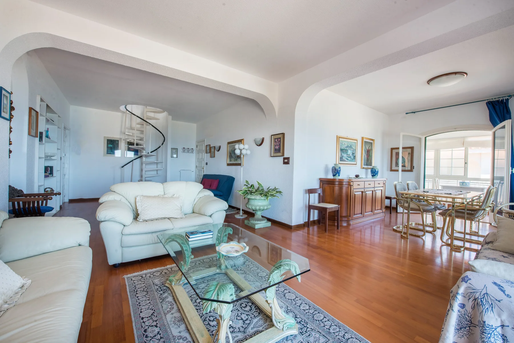 A bright living room with seating, a glass coffee table, and an adjoining dining area.
