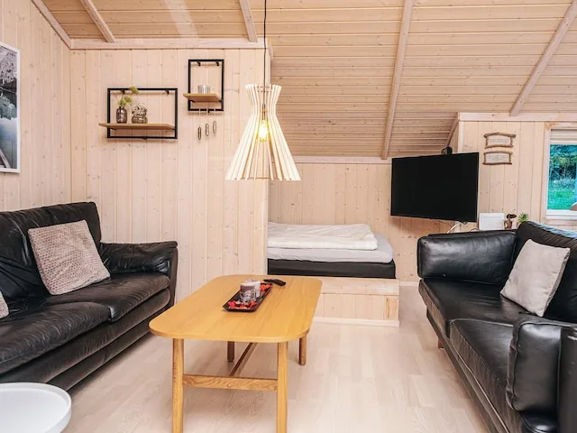 A living room with black seating, a wooden table, and a bed in the back.
