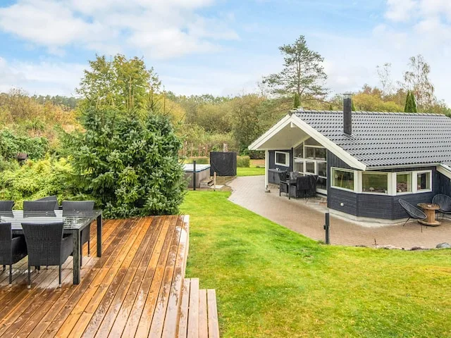 A holiday house with a wooden deck and lawn in a leafy garden.