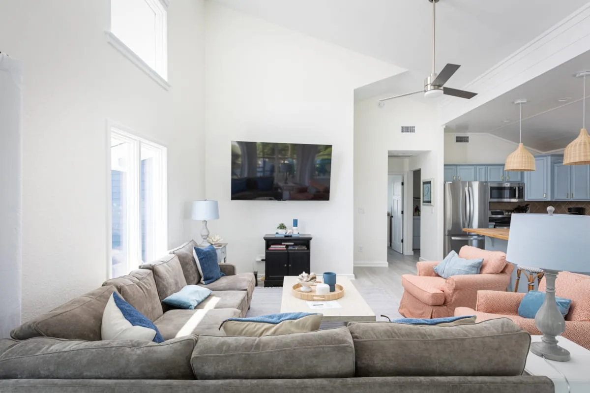 Una sala luminosa se abre a una cocina, con sofás y un televisor en la pared.
