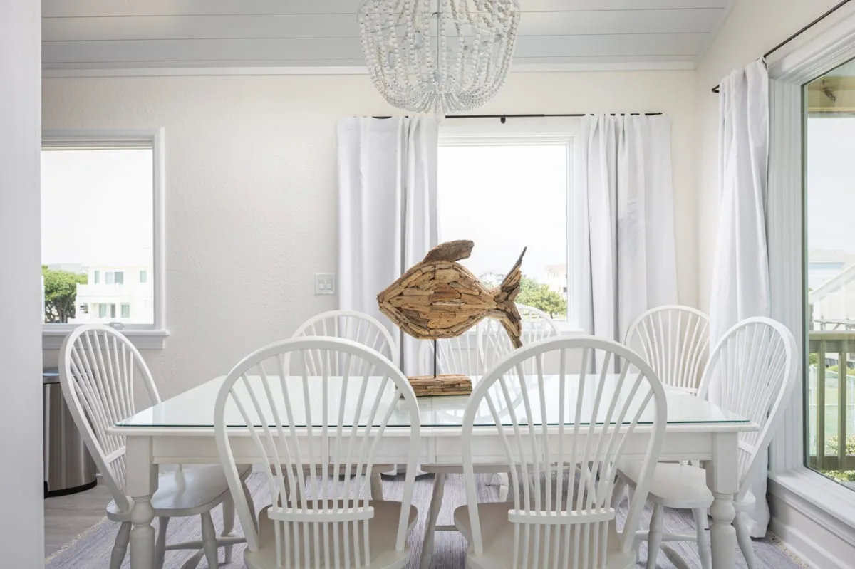 Un comedor luminoso con una mesa blanca, sillas y una escultura de pez de madera.