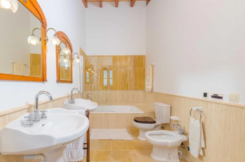 Un baño con lavabos, bañera, inodoro y paredes revestidas de madera clara.