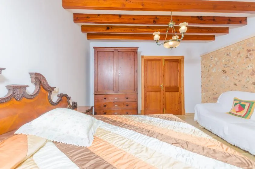 Un dormitorio con una cama grande, un armario de madera y una zona de estar cubierta de blanco.
