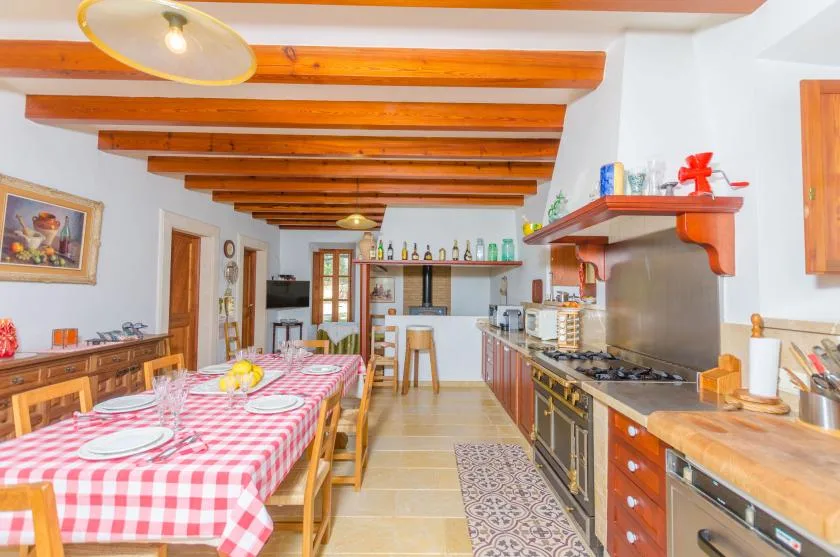Una cocina y zona de comedor rústicas con una mesa larga cubierta con un mantel a cuadros rojos y blancos.