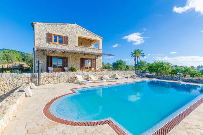Una casa de piedra da a una piscina rodeada por un patio soleado.