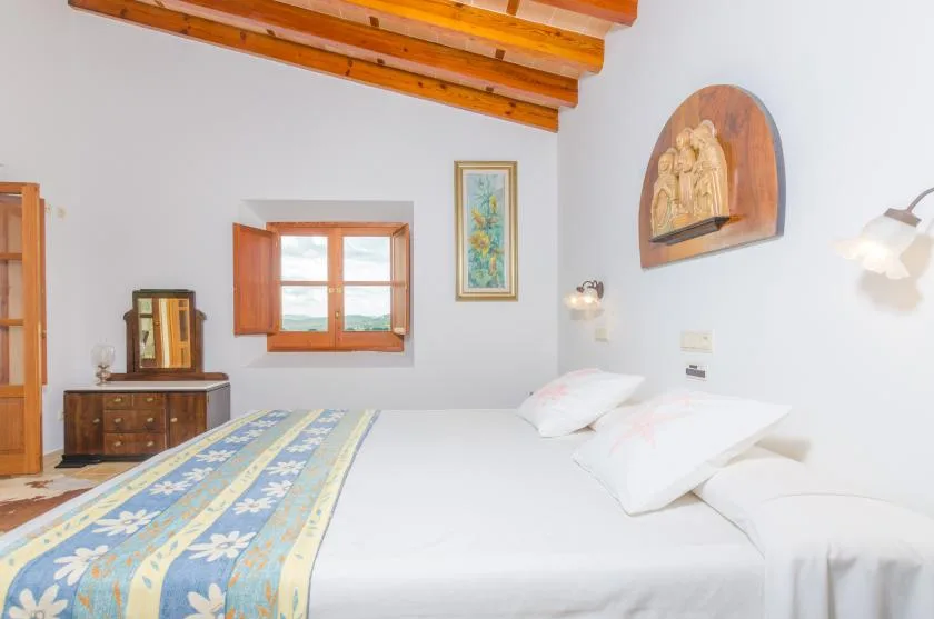 Un dormitorio con una cama, una ventana de madera y vigas expuestas en el techo.
