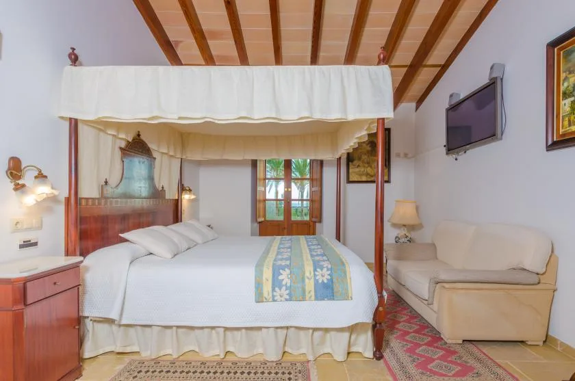 Dormitorio con cama con dosel, una pequeña zona de estar y una ventana.